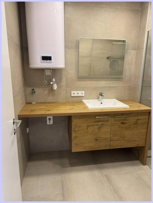 Badezimmer mit Holzwaschtisch, Spiegel und Warmwasserboiler, funktional und hell.