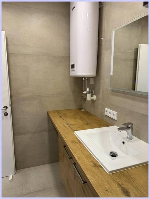 Badezimmer mit Waschtisch, Holzunterschrank und Warmwasserboiler, praktisch und stilvoll.