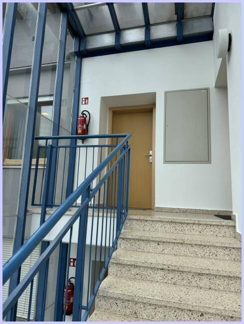 Helles Treppenhaus mit Steinstufen, blauem Geländer und Zugang zu den Wohneinheiten.