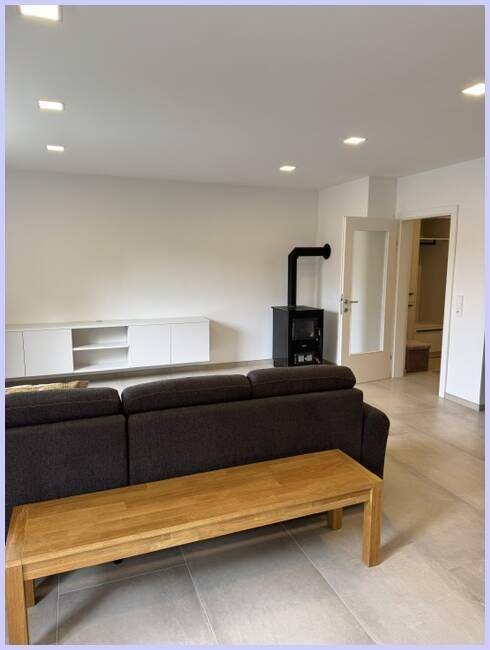 Gemütliches Wohnzimmer mit modernem Holzofen, Sofa und weißem Medienschrank.