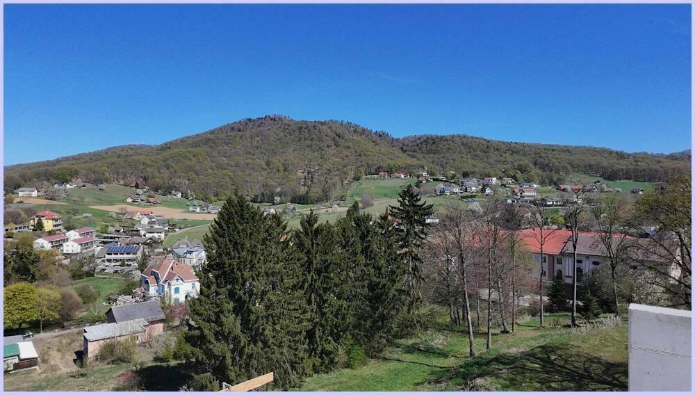 Weitläufiger Blick über eine grüne, hügelige Landschaft mit vereinzelten Häusern und Bäumen.