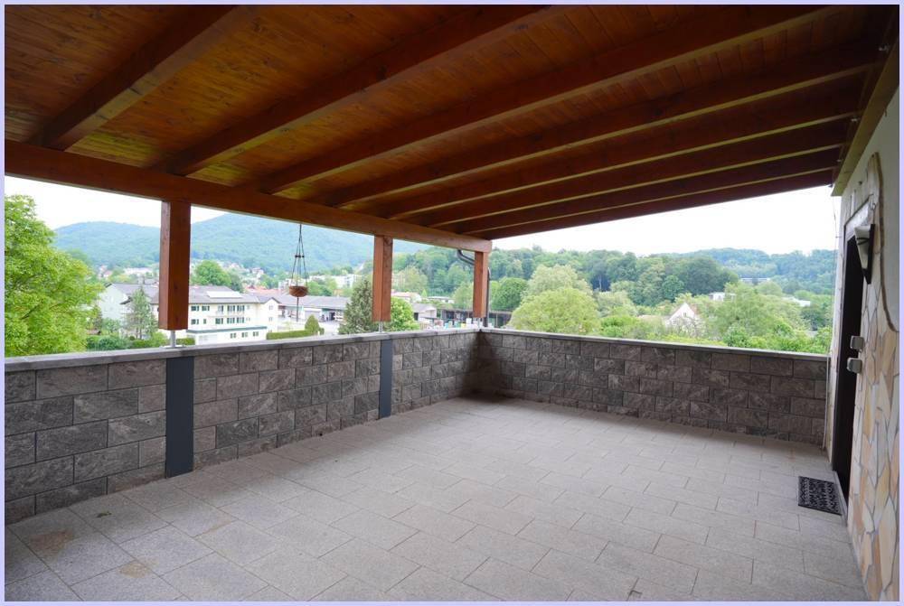 Weitläufige überdachte Terrasse mit Steinmauern und Holzbalkendecke, bietet Panoramablick.