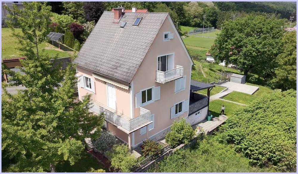 Ansicht des Hauses von oben mit Balkonen, Garten und der umliegenden grünen Landschaft.