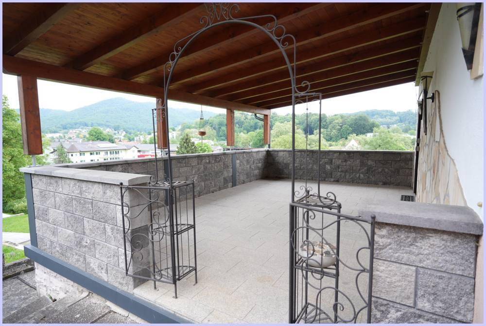 Überdachte Terrasse mit Steinmauern und schmiedeeisernem Tor, bietet weiten Blick ins Grüne.