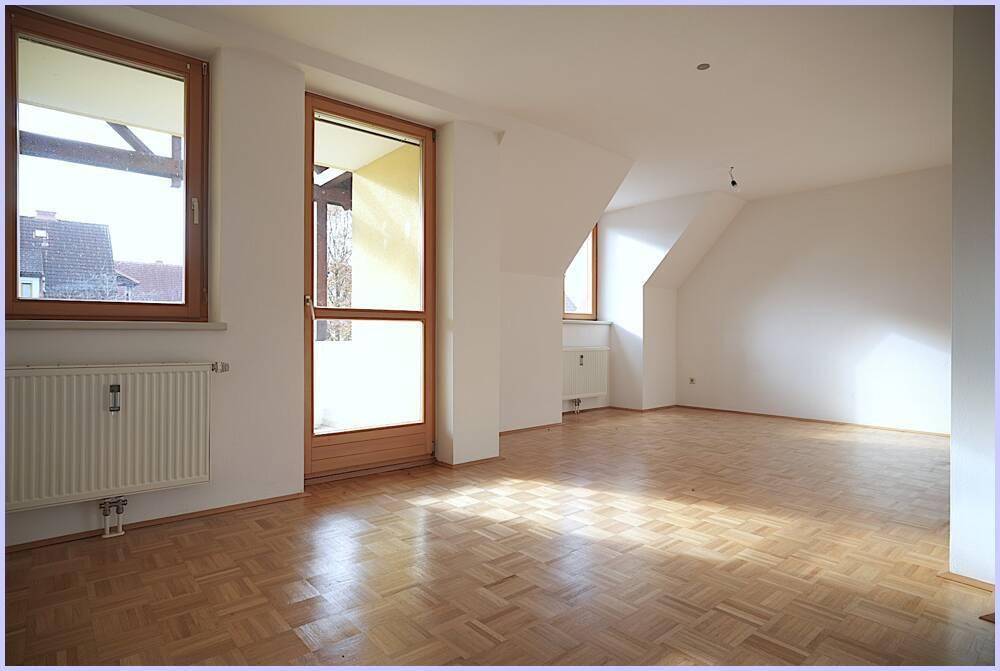 Helles, leeres Zimmer mit Parkettboden, Dachschrägen und Zugang zum Balkon.