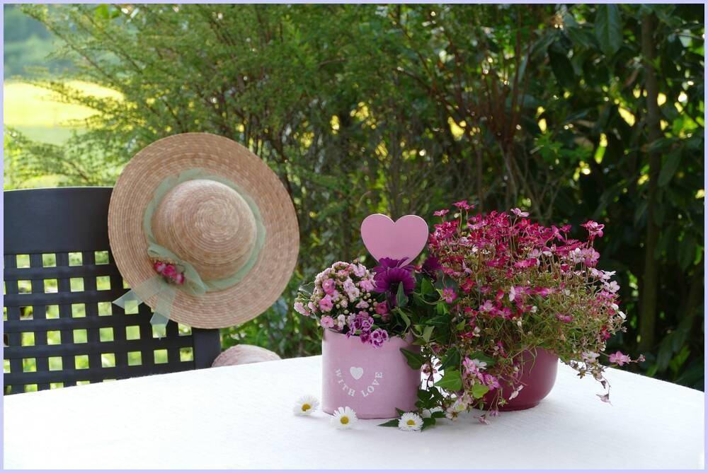 Gemütliche Gartendekoration mit Strohhut, bunten Blumen und Gänseblümchen auf einem Tisch.