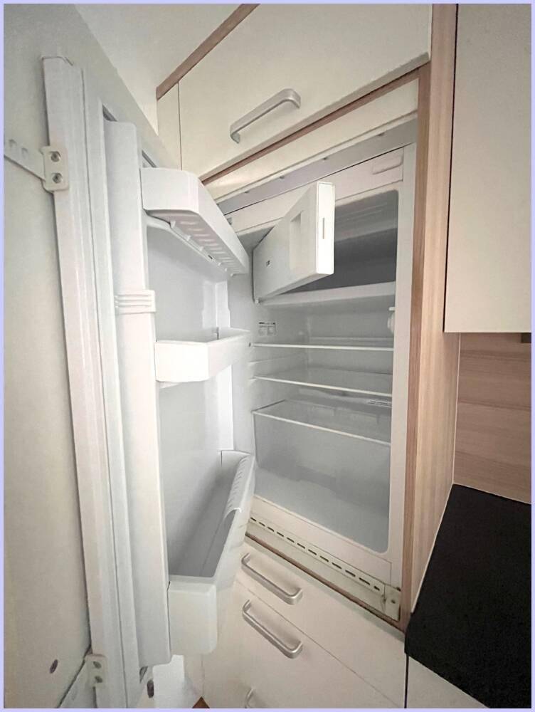 Integrierter Kühlschrank in der Küche mit geöffneter Tür und mehreren Ablagefächern.