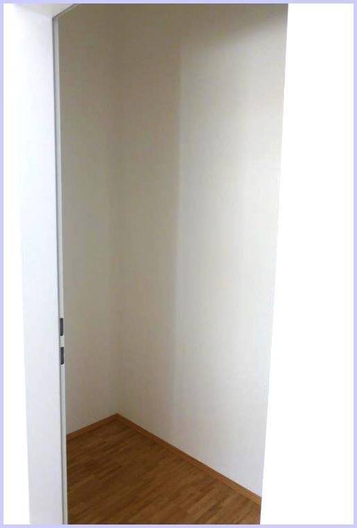 Kleiner Abstellraum oder begehbarer Schrank mit Holzboden und weißen Wänden.
