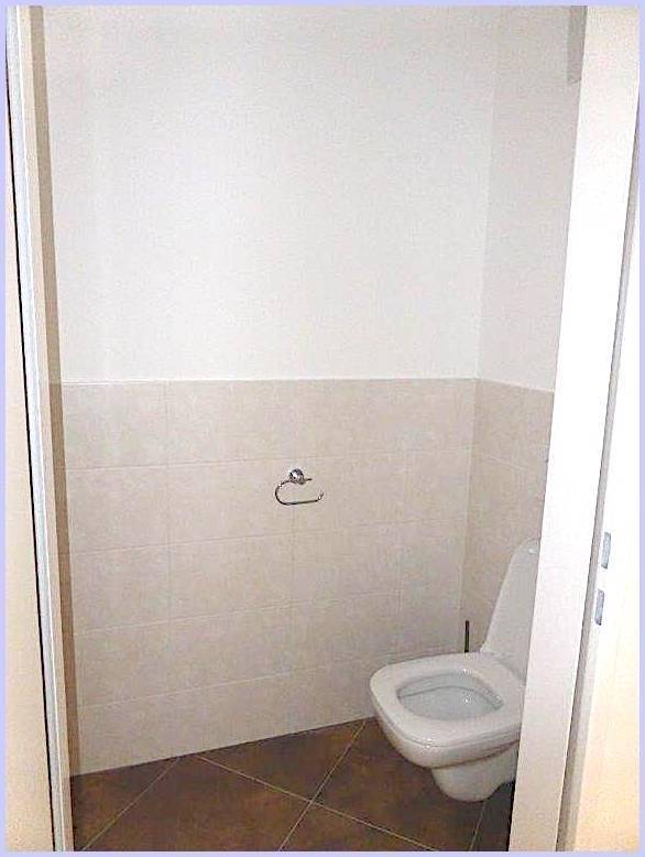 Kleines WC mit wandhängender Toilette und hellen Fliesen an den Wänden.
