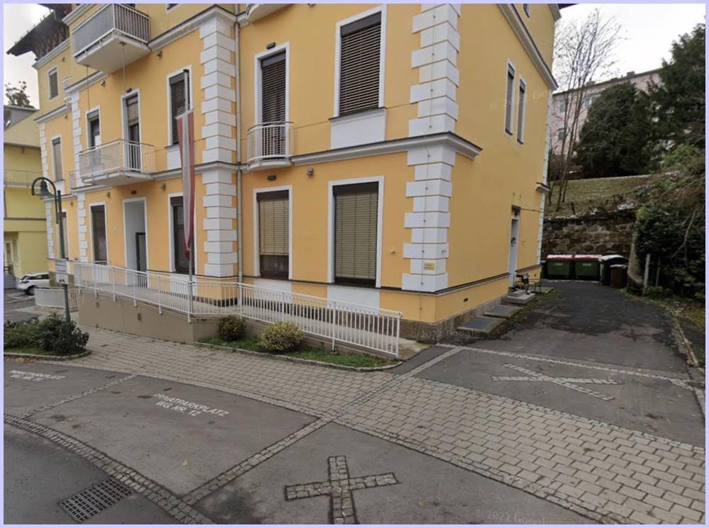 Gelbes Gebäude mit klassischer Architektur, Balkonen und einer barrierefreien Rampe am Eingang.