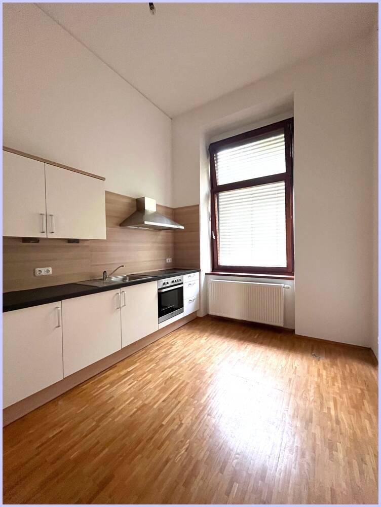 Helle Küche mit weißen Schränken, integriertem Backofen und Fenster mit Jalousien.