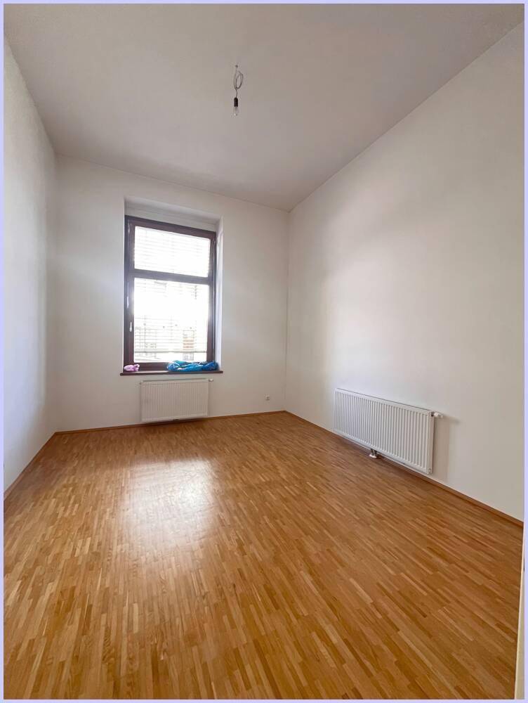 Helles Schlafzimmer mit Holzboden, weißen Wänden und einem Fenster mit Jalousien.
