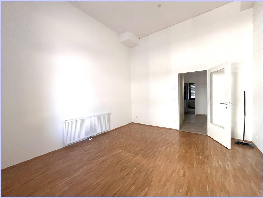 Leeres Zimmer mit hellem Holzboden, weißen Wänden und Zugang zu einem weiteren Raum.