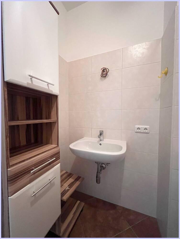 Badezimmer mit Einzelwaschbecken, hellen Fliesen und praktischem Hochschrank.