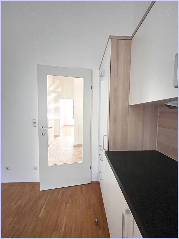 Detailansicht der Küche mit weißen Schränken, dunkler Arbeitsplatte und Glastür zum Nebenraum.