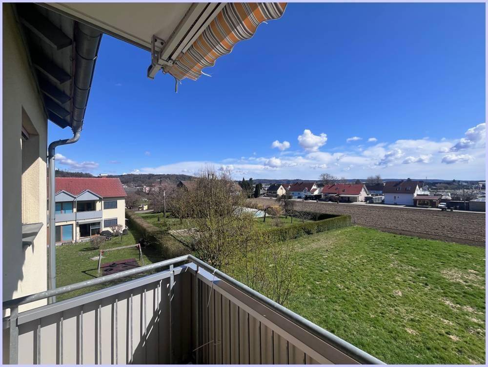 Balkon mit Blick auf grüne Wiesen und die Nachbarschaft unter blauem Himmel mit einigen Wolken.