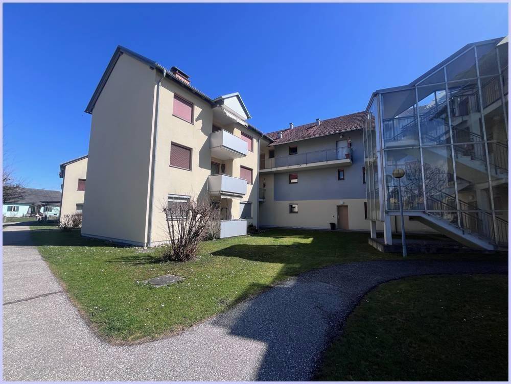 Mehrfamilienhaus mit beige gestrichener Fassade, Balkonen und einem modernen Glas-Treppenhaus im Außenbereich.
