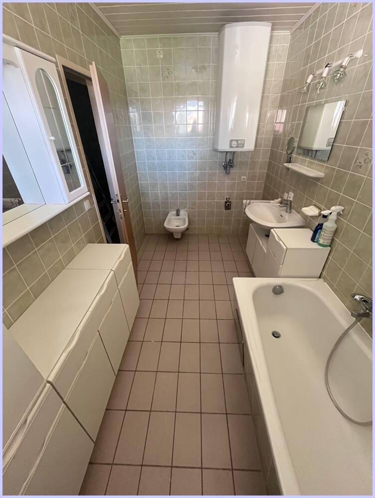 Badezimmer mit Badewanne, Waschbecken und Bidet, hell gefliest und mit einem Warmwasserboiler ausgestattet.