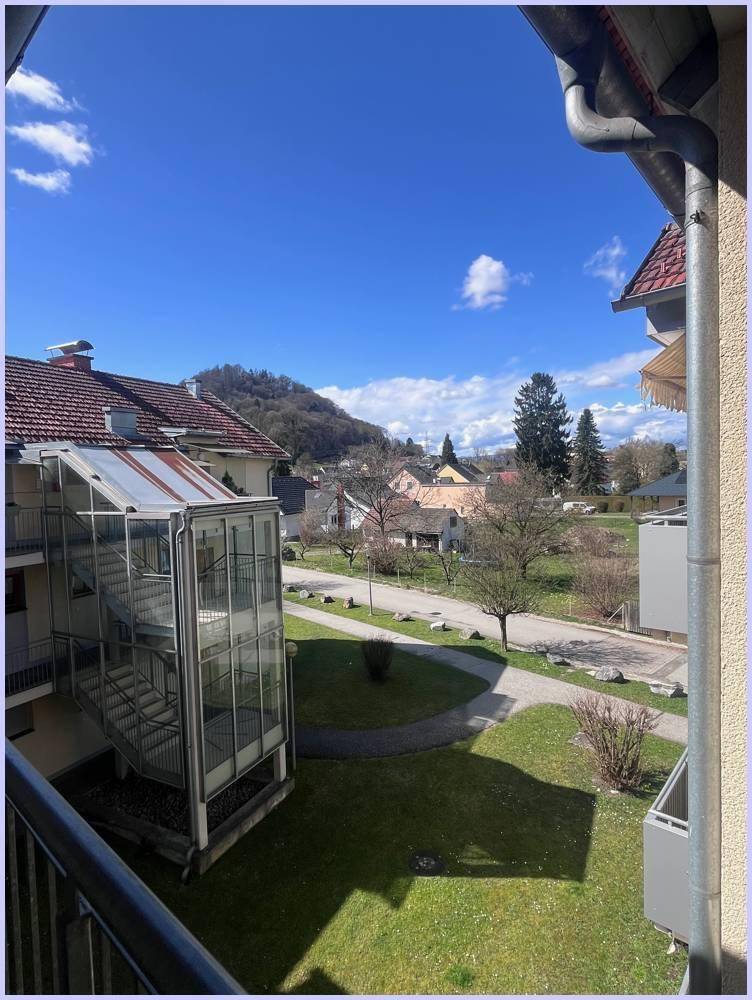 Balkonblick auf das moderne Glas-Treppenhaus, grüne Rasenflächen und die hügelige Landschaft im Hintergrund.