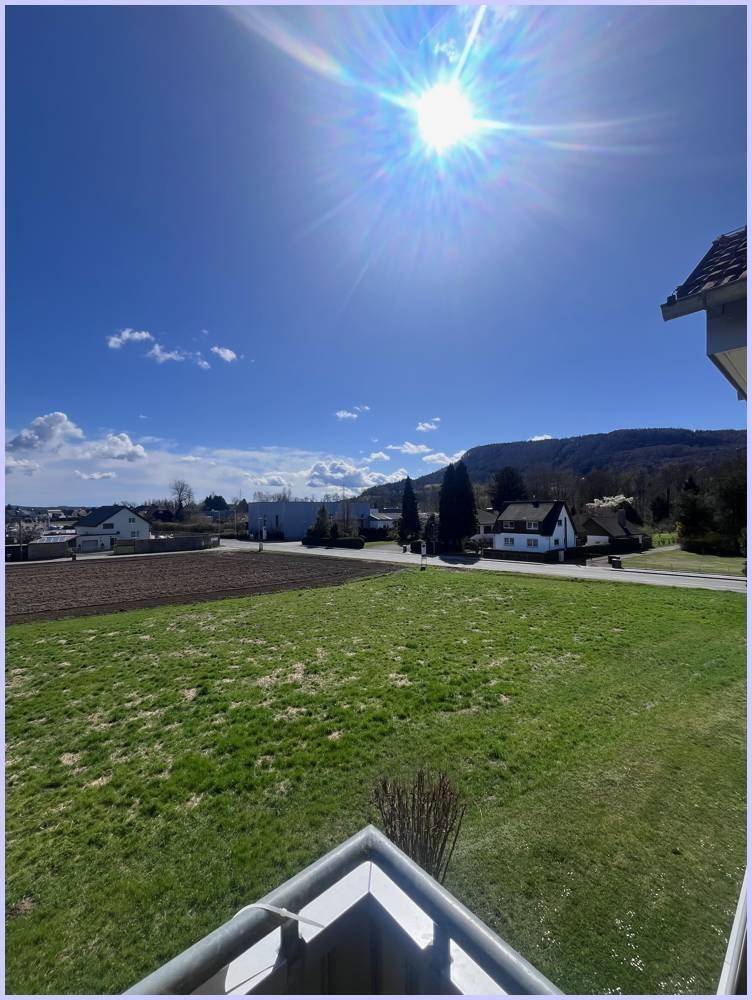 Sonniger Balkon mit weitem Blick über grüne Felder und die hügelige Landschaft unter strahlend blauem Himmel.