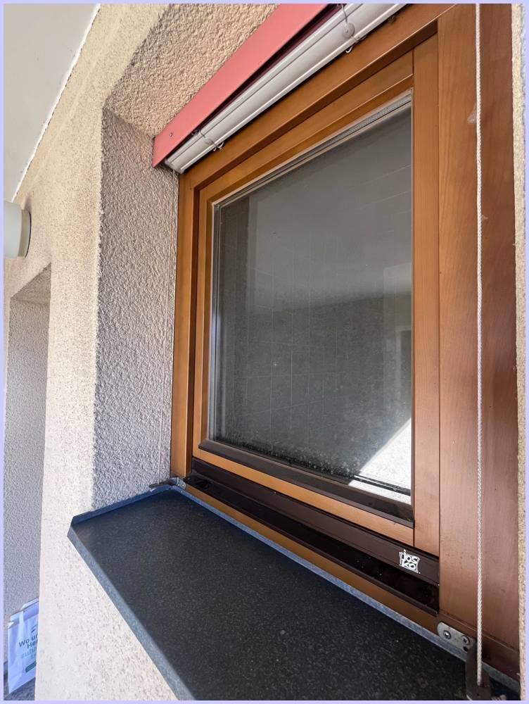 Detailansicht eines Fensters mit Holzrahmen und Außenjalousie, eingebettet in die Fassade.