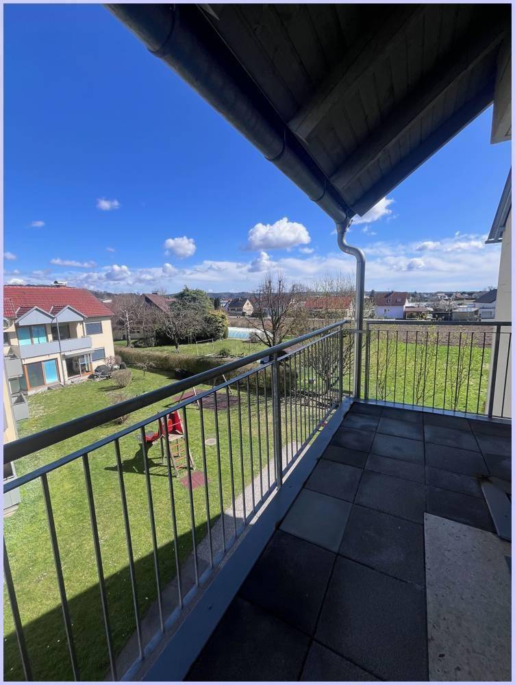 Balkon mit Fliesenboden und Blick auf einen Spielplatz sowie grüne Wiesen und die umliegende Bebauung.