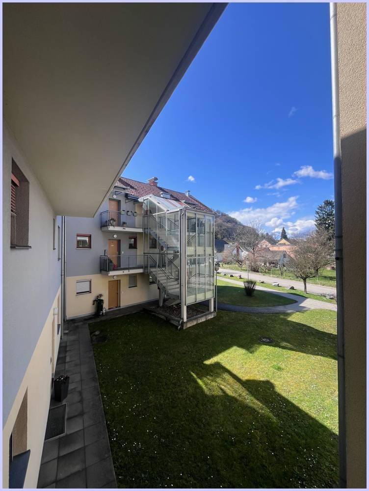 Blick auf das Mehrfamilienhaus mit Glas-Treppenhaus und grüner Rasenfläche, umgeben von Natur.