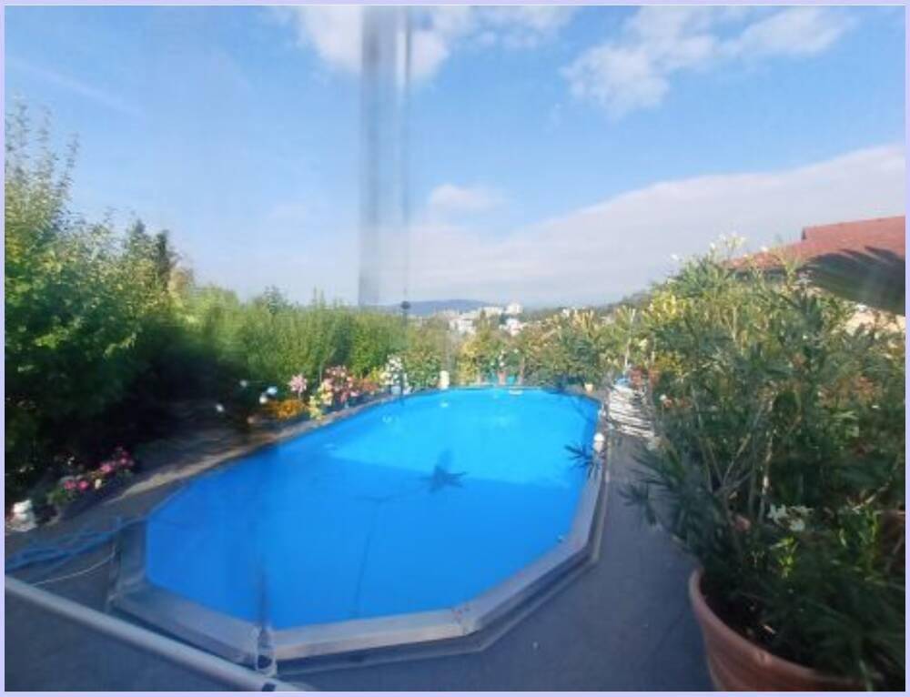 Außenpool mit blauer Abdeckung, umgeben von Pflanzen und mit Fernblick über die Umgebung.