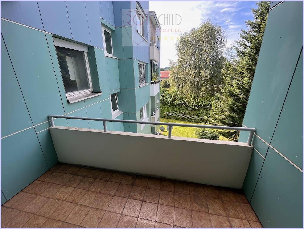 Geräumiger Balkon mit Fliesenboden und Blick auf den Gemeinschaftsgarten und die Umgebung.