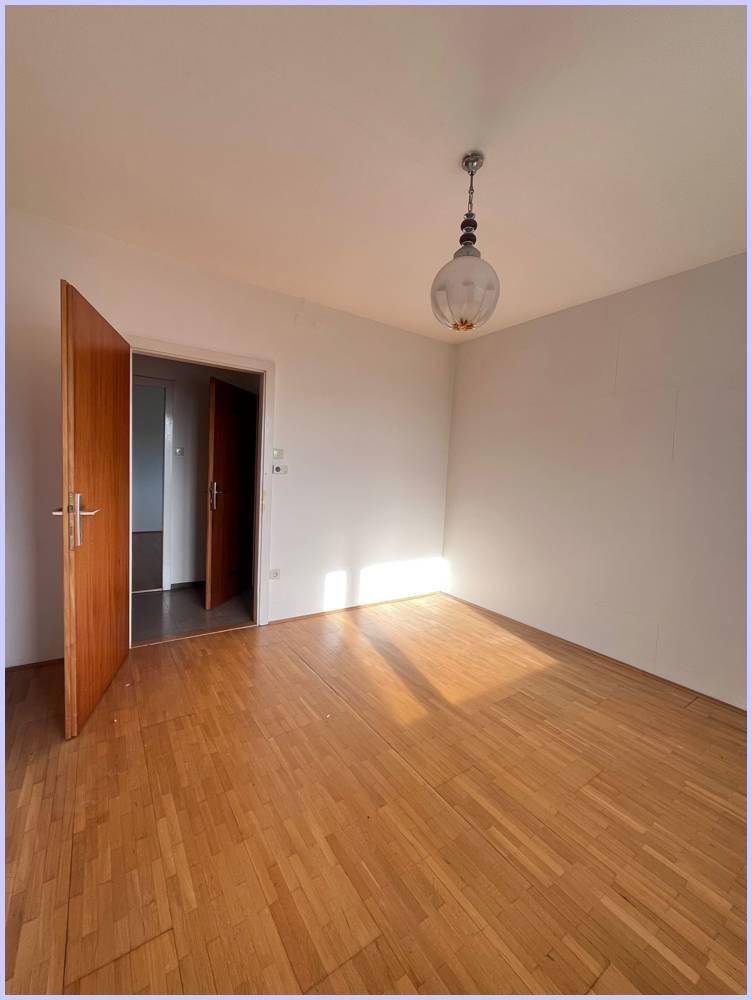 Sonniger Raum mit Holzboden und einer Pendelleuchte, der viel natürliches Licht erhält.