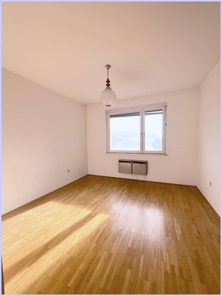 Helles Zimmer mit Holzboden und großem Fenster, das viel Sonnenlicht hereinlässt.
