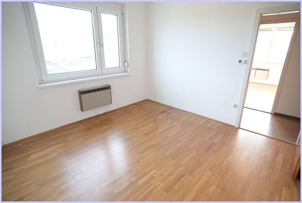 Geräumiges Zimmer mit Holzboden und Fenster, das zu einem weiteren Raum führt.