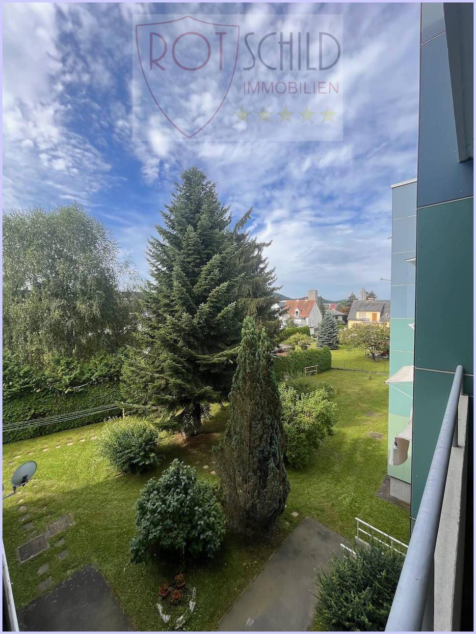 Blick auf den gepflegten Gemeinschaftsgarten mit Rasenflächen und hohen Bäumen.