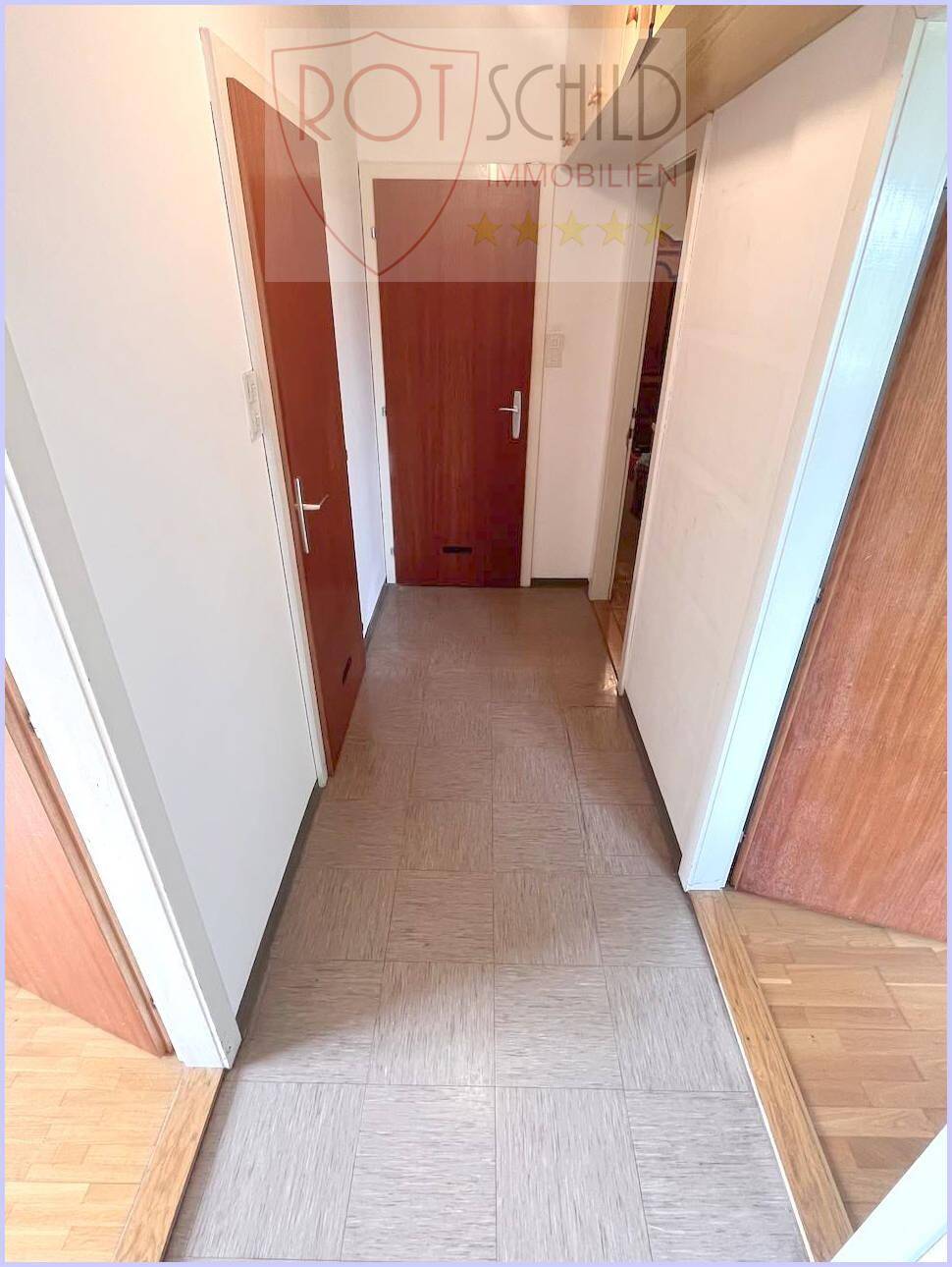 Langer Flur mit Fliesenboden und mehreren Holztüren, der verschiedene Räume verbindet.