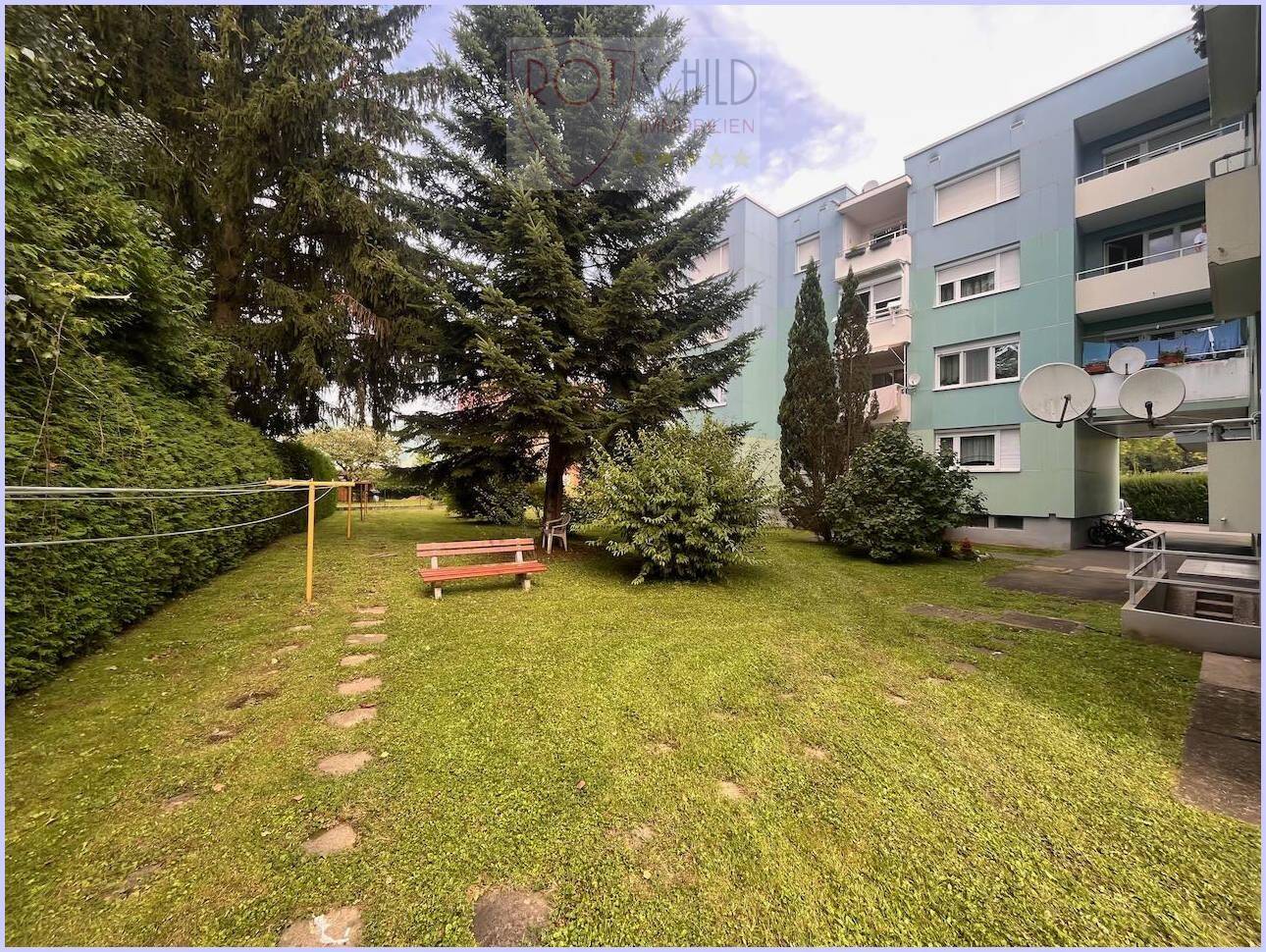 Gepflegter Gemeinschaftsgarten mit Rasen, Bäumen und einer Holzbank zum Entspannen.