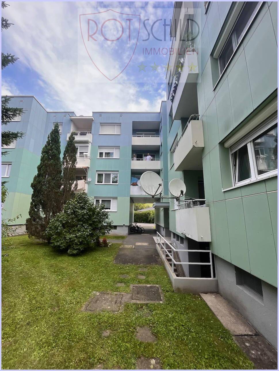 Ansicht des Wohngebäudes mit Gemeinschaftsrasenfläche und Zugang zu den Eingängen.