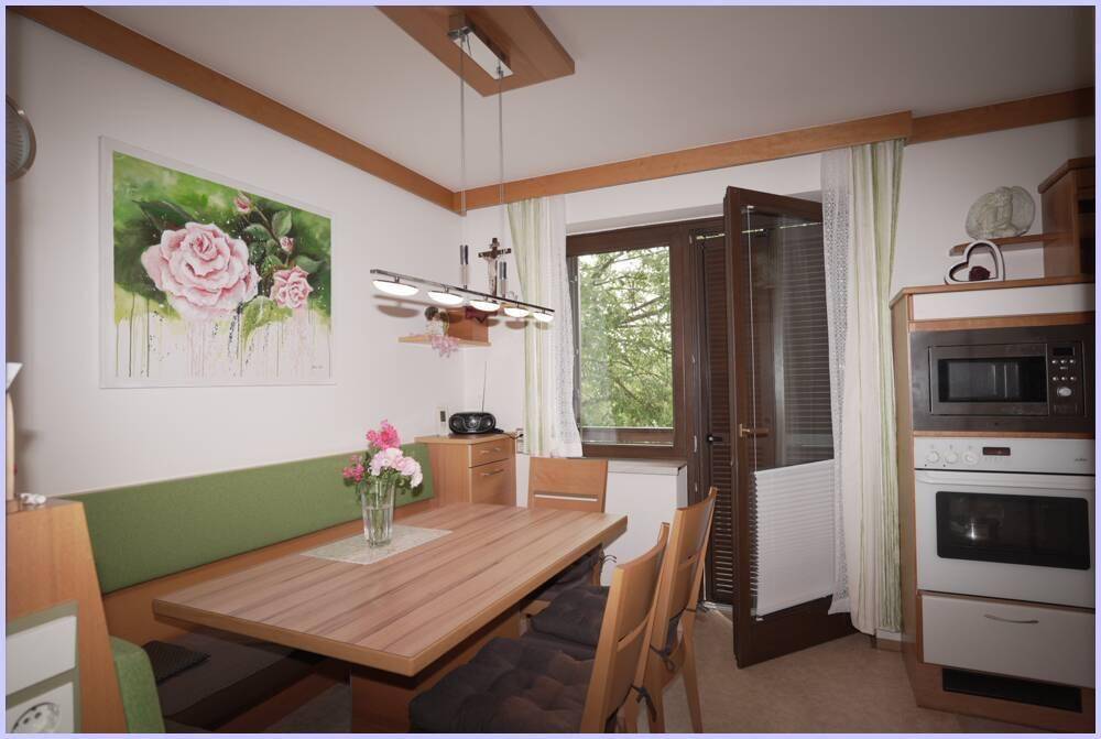 Essbereich in der Küche mit Holztisch und Eckbank, daneben ein Fenster mit Blick auf die Natur.