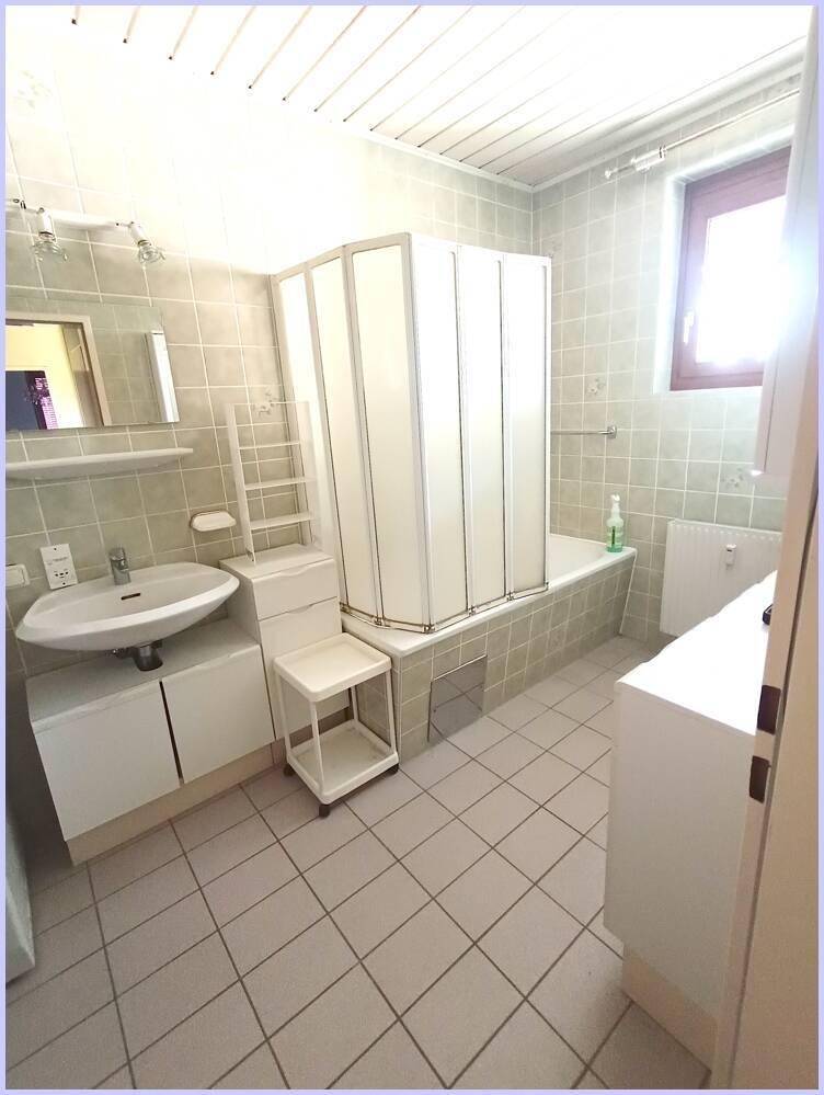 Helles Badezimmer mit Badewanne, Duschkabine, Waschbecken und Fenster.