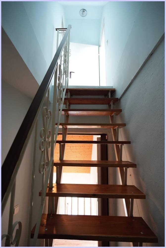 Holztreppe mit dekorativem Metallgeländer, die in die obere Etage führt.