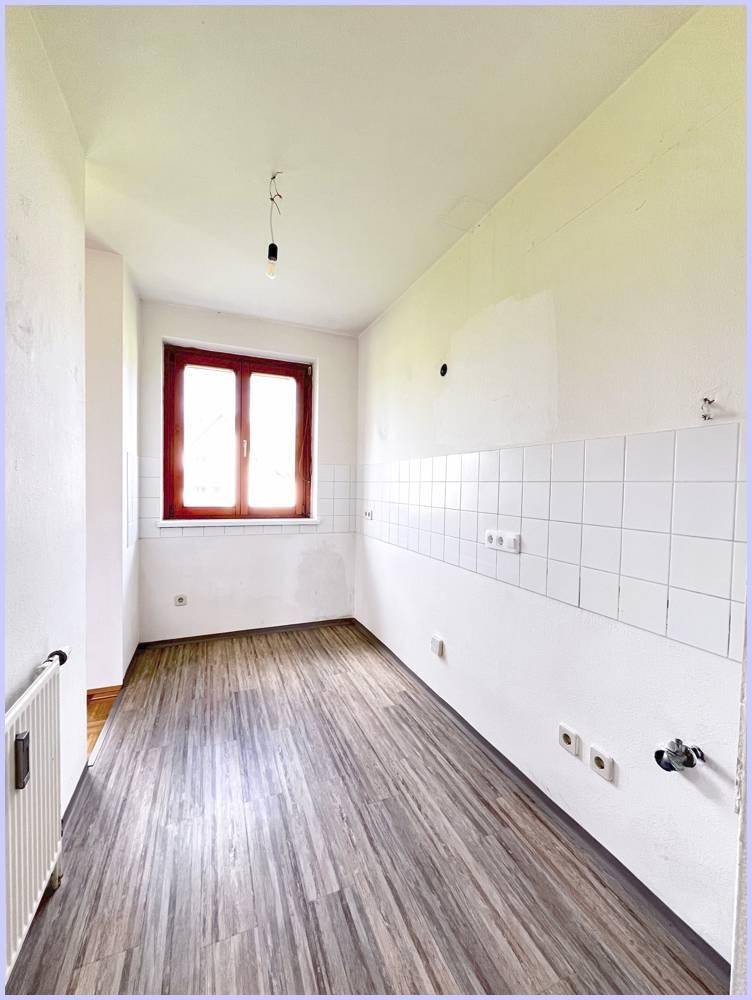 Leere Küche mit Laminatboden, weißen Fliesen und Fenster für natürliches Licht.
