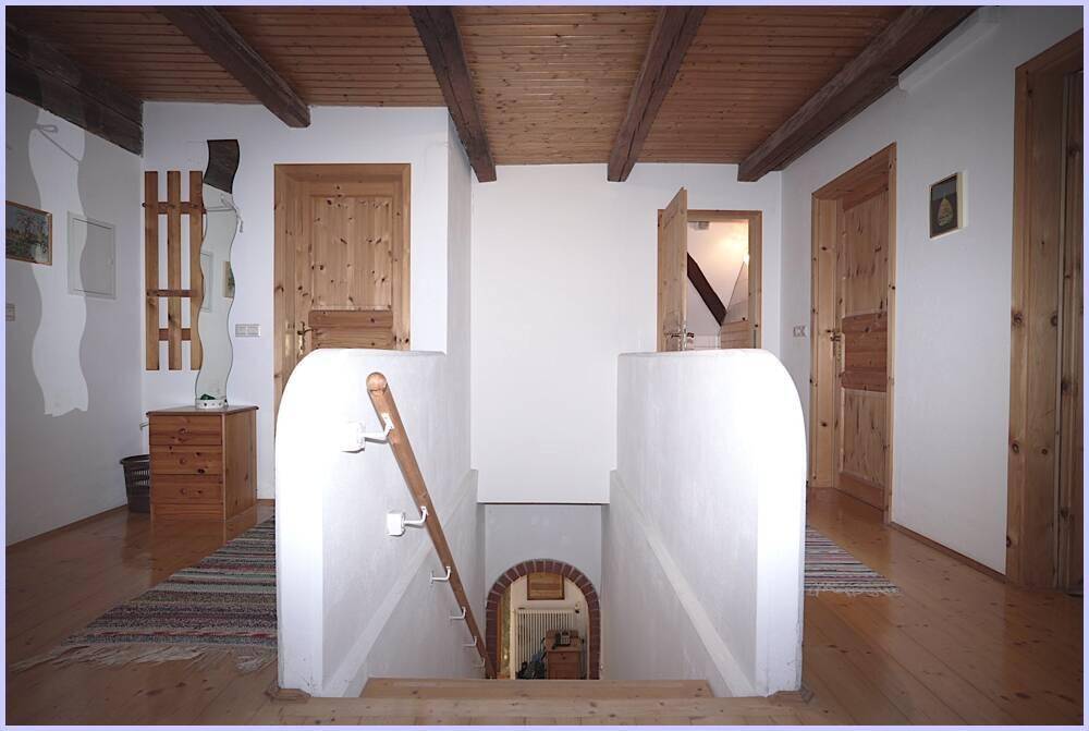 Heller Flurbereich im Obergeschoss mit Holzboden, sichtbaren Holzbalken und einer Treppe ins Untergeschoss.