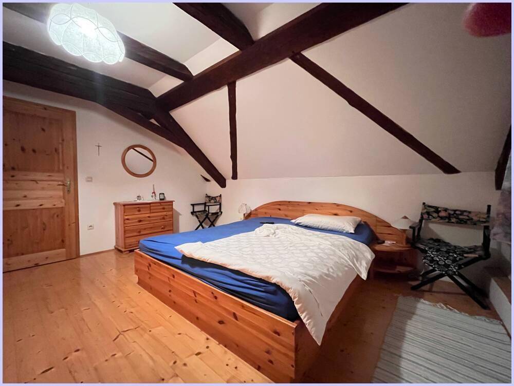 Gemütliches Schlafzimmer im Dachgeschoss mit Holzboden, sichtbaren Holzbalken und einem Doppelbett.