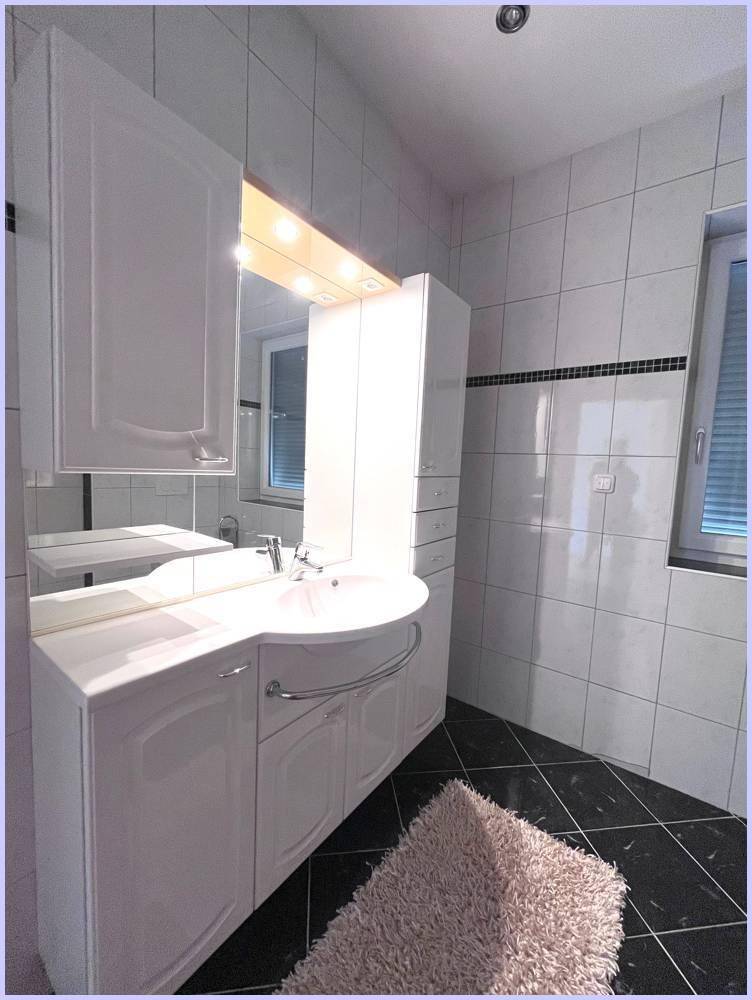 Modernes Badezimmer mit weißem Waschtisch, Spiegelschrank und Fenster.