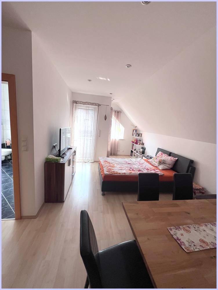 Schlafzimmer im Dachgeschoss mit Dachschräge, Holzboden und Balkonzugang.