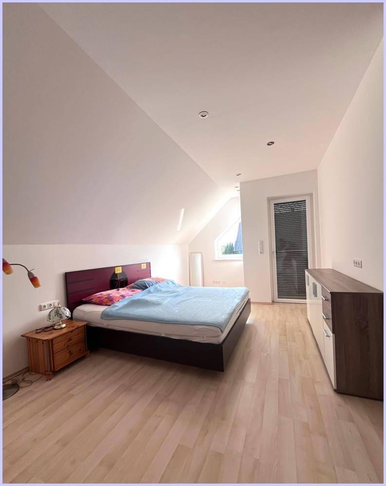 Helles Schlafzimmer im Dachgeschoss mit Bett, Kommode und Fenster mit Rollladen.