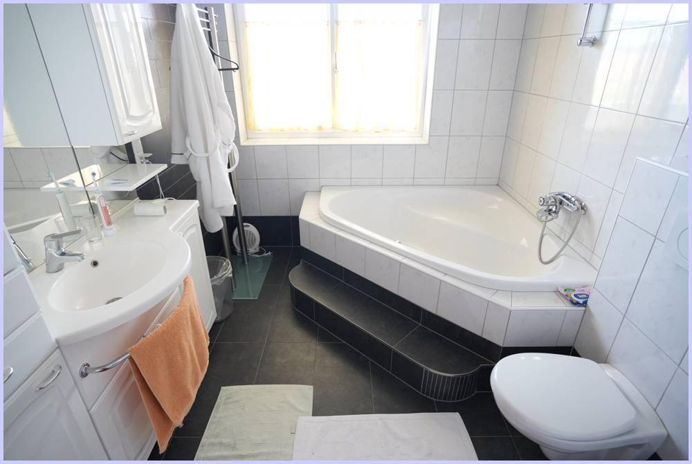 Badezimmer mit Eckbadewanne, WC, Waschbecken und Fenster.