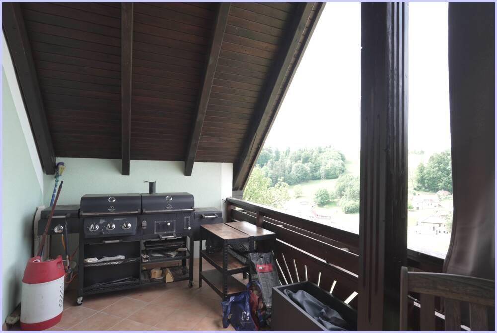 Geräumiger Balkon mit Grillstation, Holzboden und weitem Blick ins Grüne.