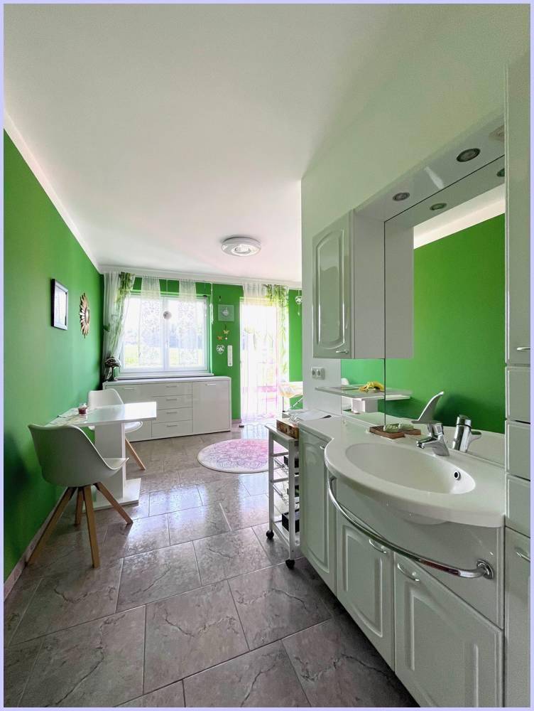 Helles Arbeitszimmer mit grünen Wänden, Fliesenboden und Blick in den Garten.