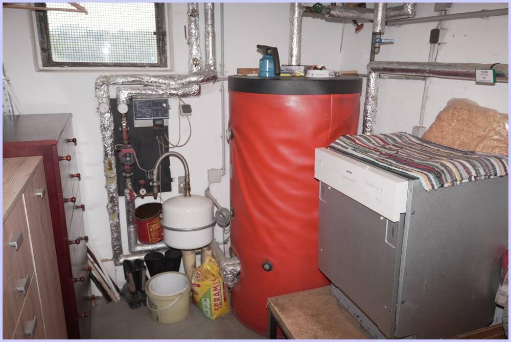 Technikraum mit großem Warmwasserspeicher, Rohren und Waschmaschine.