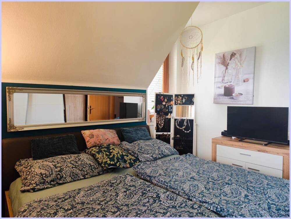 Gemütliches Schlafzimmer mit Doppelbett, Spiegel und Dachschräge.